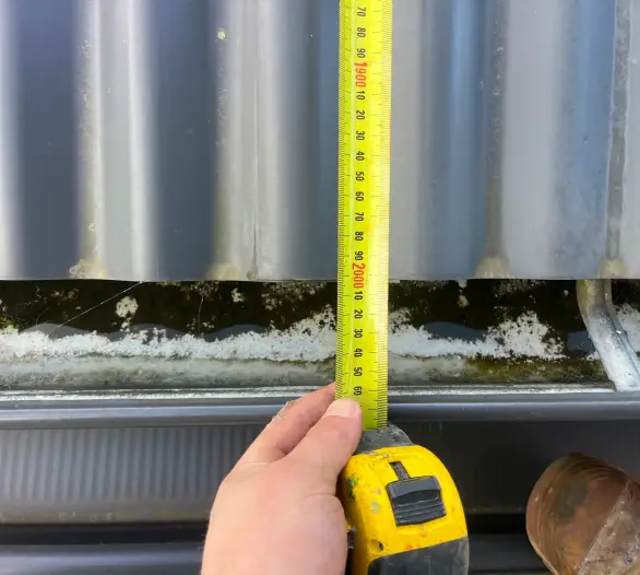 Hand holding a tape measure against a roof gutter
