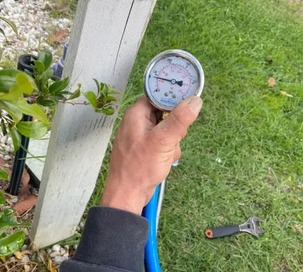Hand holding a water pressure gauge connected to an outdoor tap fitting