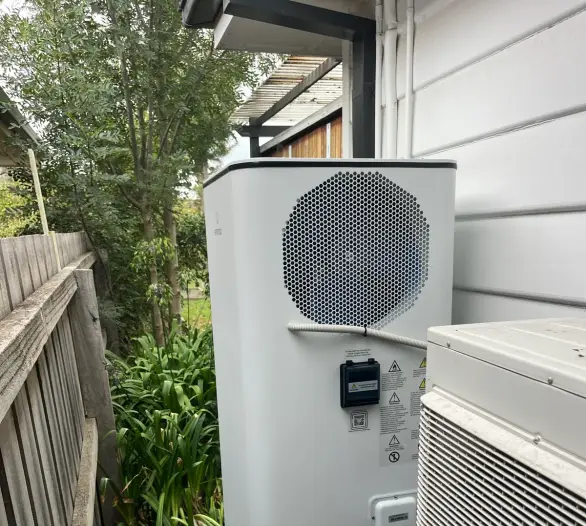 Heat pump hot water cylinder and outdoor unit in a side passage