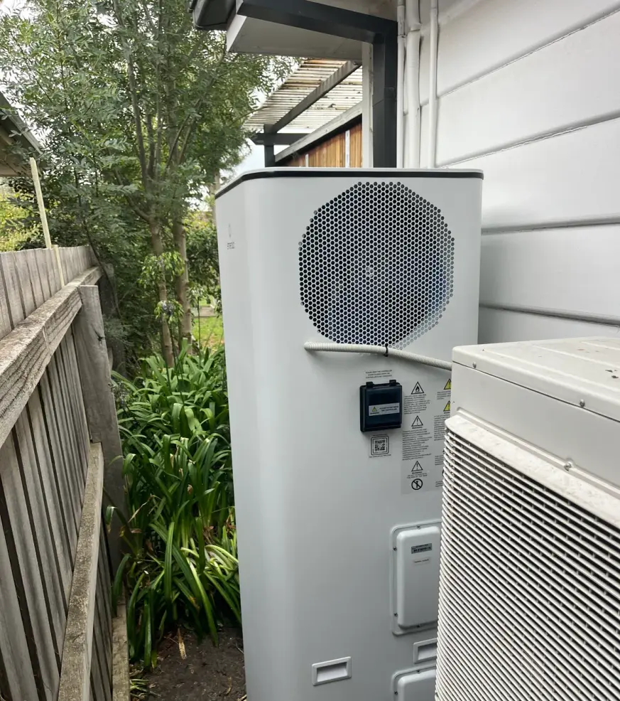 Heat pump hot water cylinder and outdoor unit in a side passage