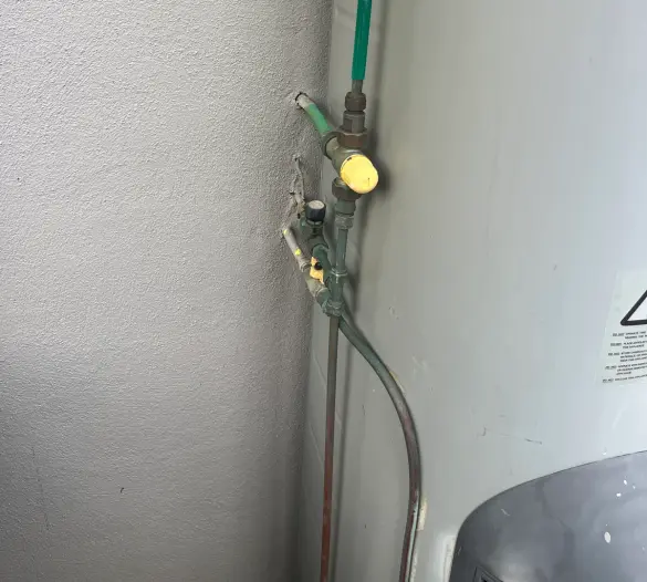 Hot water unit beside a wall with a gas valve and pipework