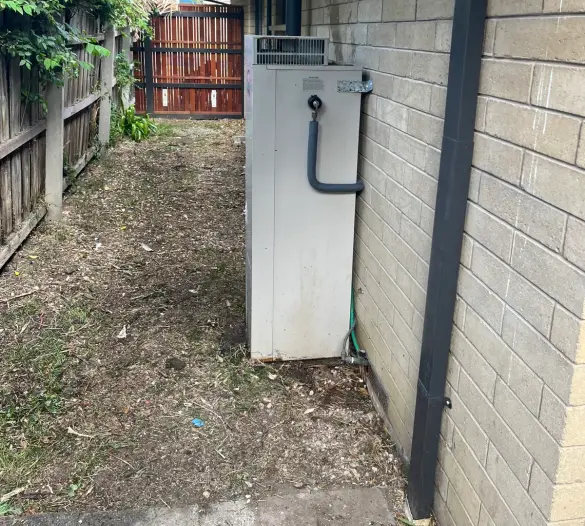 Hot water unit in a narrow side passage beside a brick wall and a dark downpipe