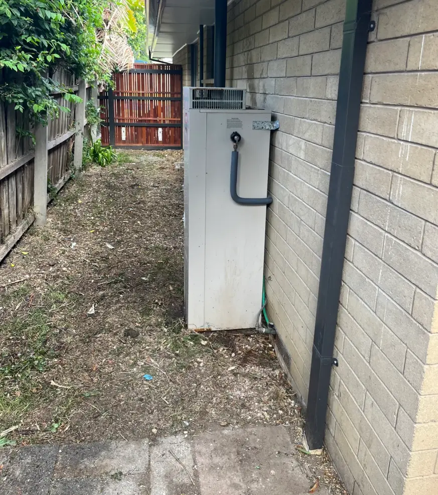 Hot water unit in a narrow side passage beside a brick wall and a dark downpipe