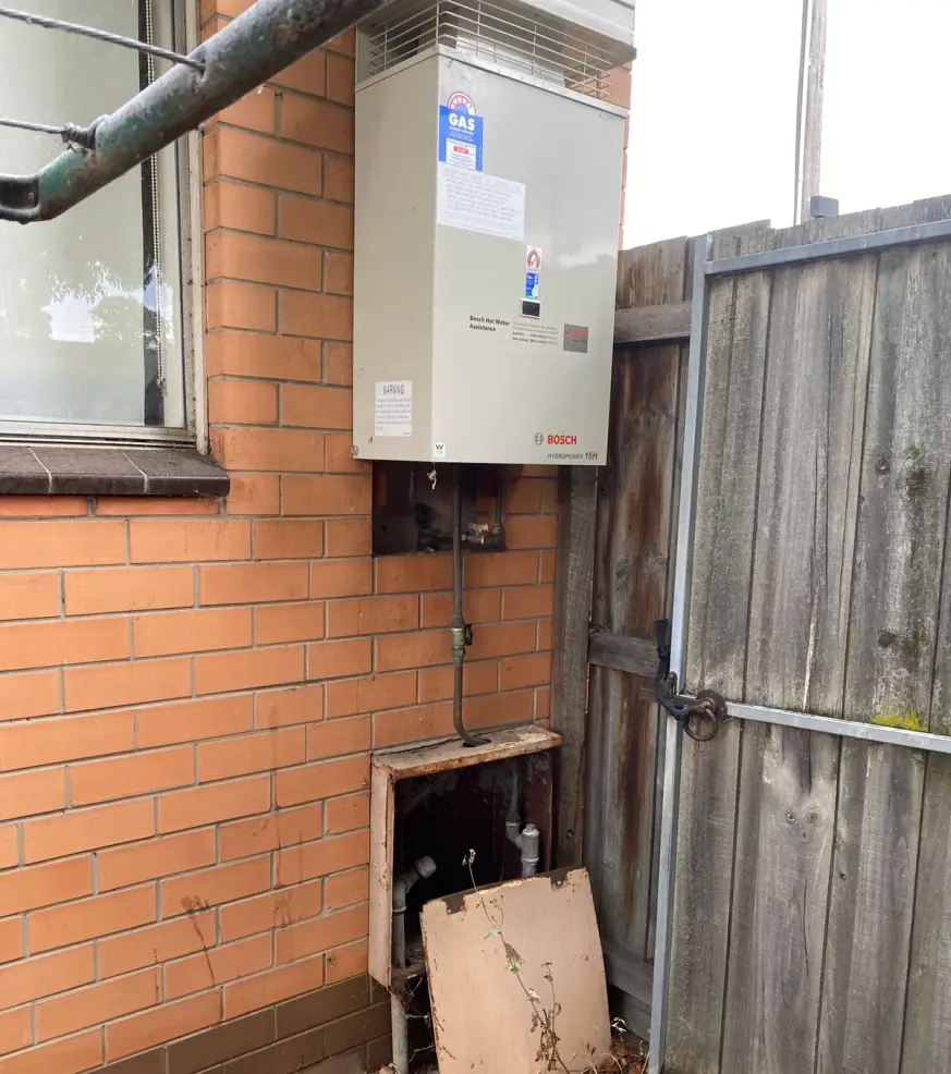 Hot water unit on an orange brick wall beside a gate and a cabinet