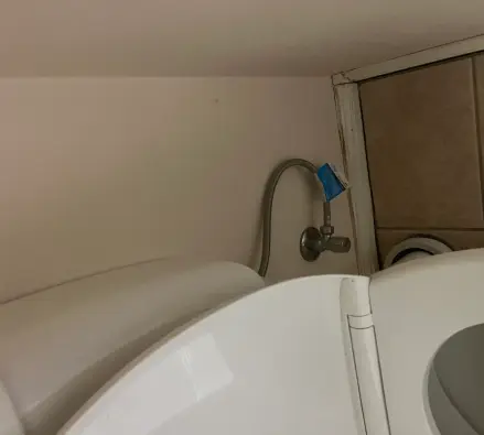 Isolation tap and flexible hose at the base of a toilet, with a blue tag on the pipe