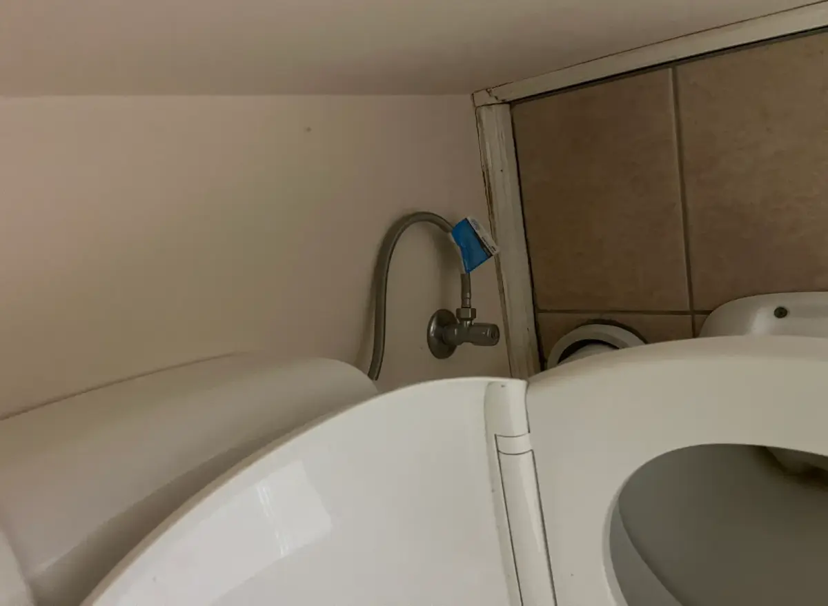 Isolation tap and flexible hose at the base of a toilet, with a blue tag on the pipe