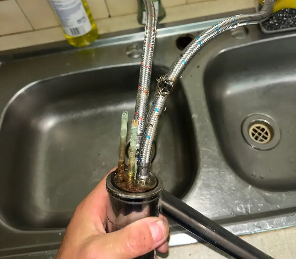Kitchen tap lifted out of a double sink with its braided hoses still attached