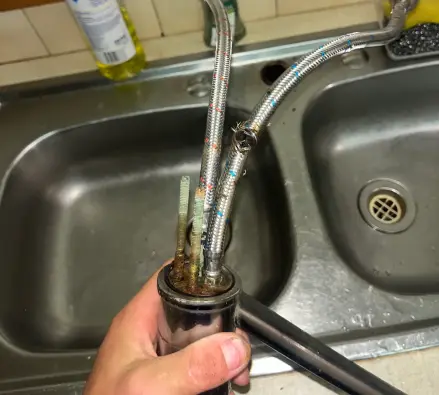 Kitchen tap lifted out of a double sink with its braided hoses still attached