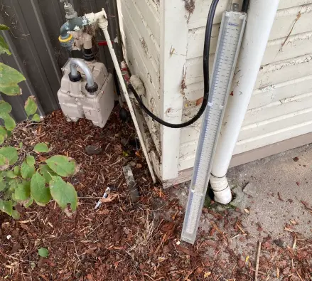Manometer connected to a gas meter beside a weatherboard wall with pliers nearby