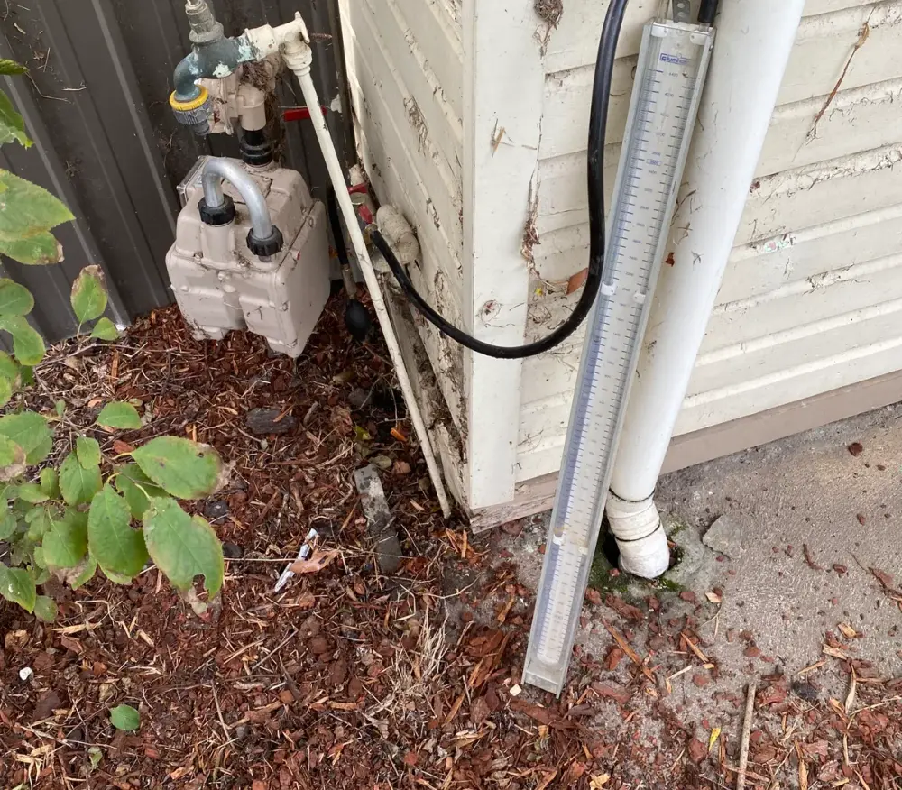 Manometer connected to a gas meter beside a weatherboard wall with pliers nearby