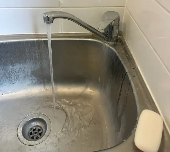 Mixer tap running water into a stainless steel laundry tub