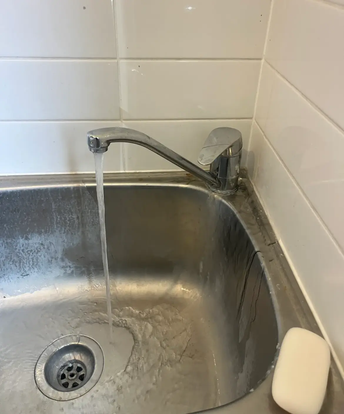 Mixer tap running water into a stainless steel laundry tub