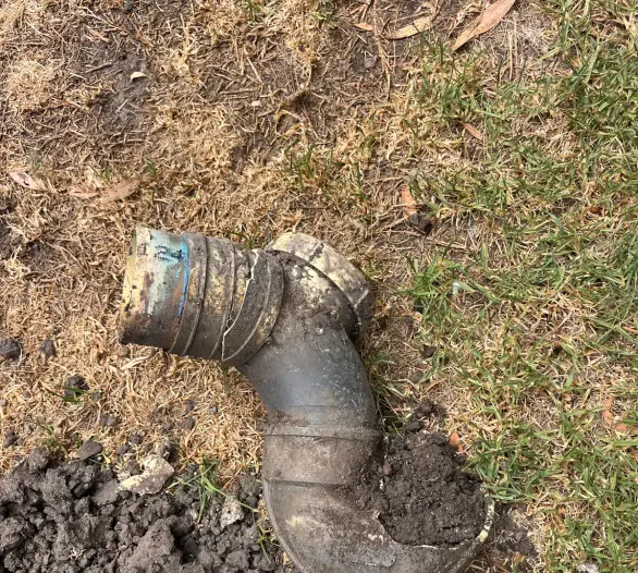 Muddy drain elbow lifted out of the ground onto grass