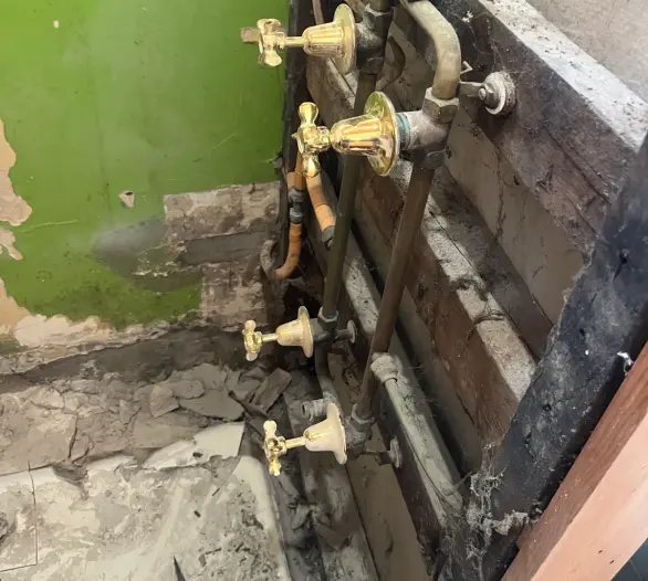 Old brass taps and copper pipework exposed in a stripped bathroom wall