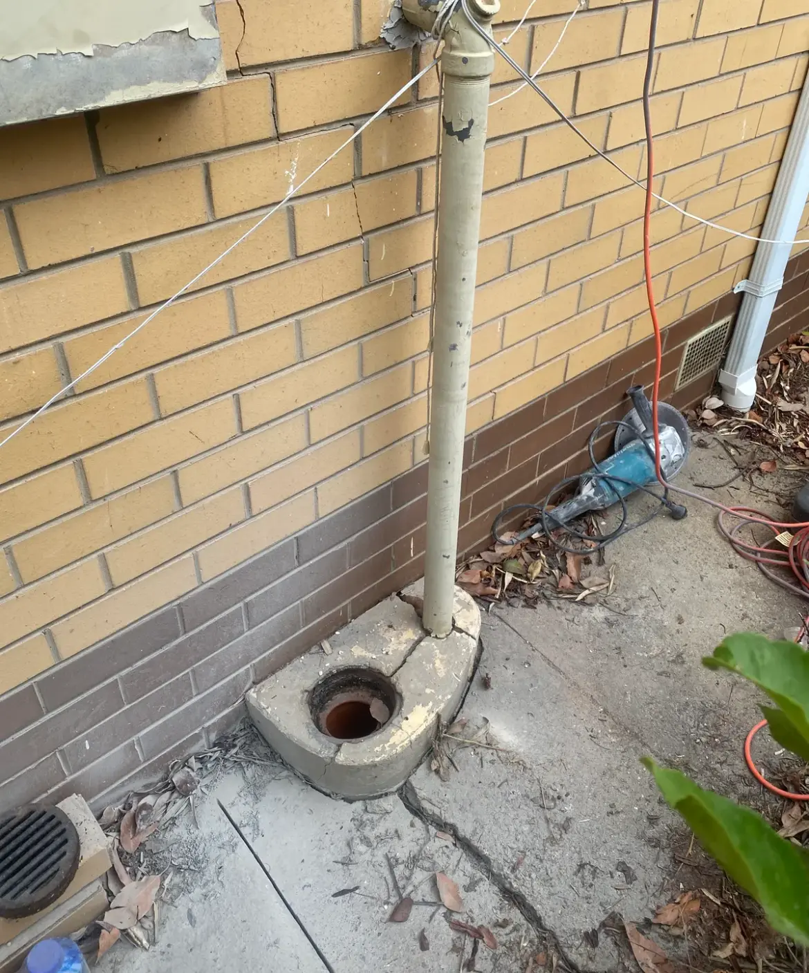 Pipe with brass fitting on a yellow brick wall above a concrete gully trap, angle grinder on the ground