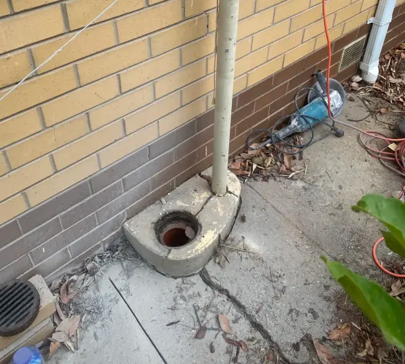 Pipe with brass fitting on a yellow brick wall above a concrete gully trap, angle grinder on the ground