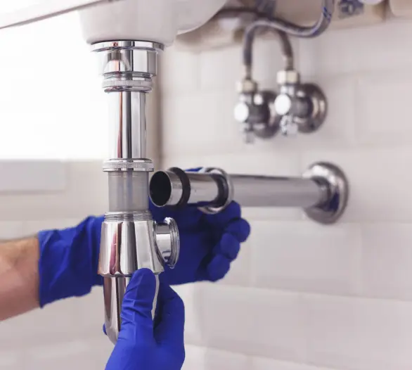 Plumber fitting a chrome bottle trap under a bathroom basin