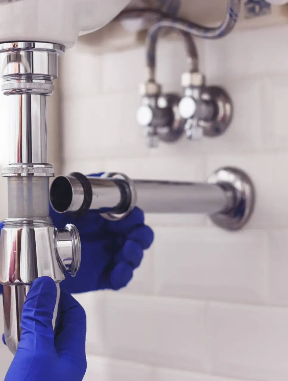 Plumber fitting a chrome bottle trap under a bathroom basin
