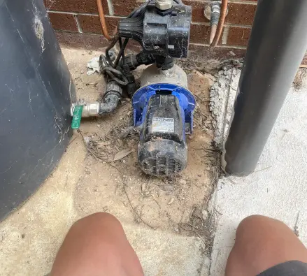 Rainwater tank pump with brass fittings and copper pipework beside a brick wall