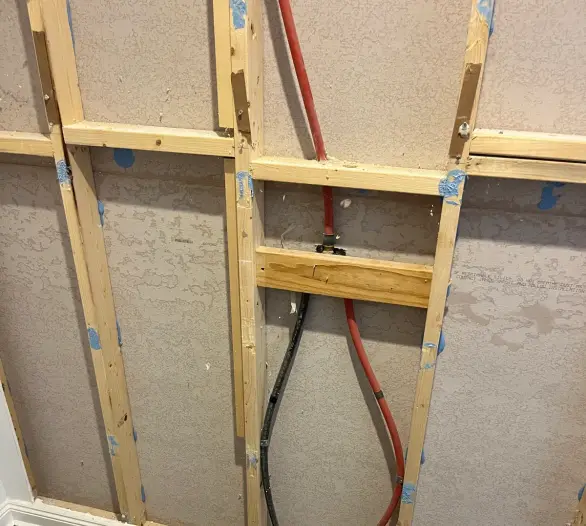 Red and black flexible water pipes inside an opened timber stud wall