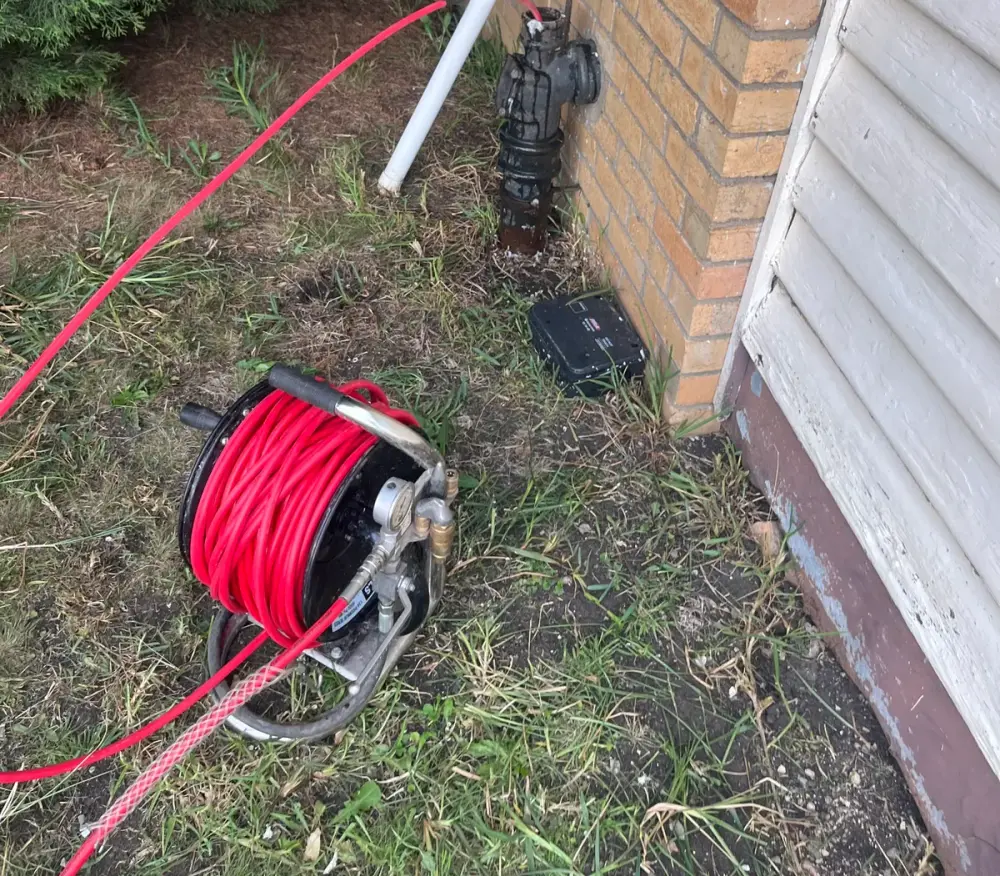Red hose reel on the ground with a hose running to a cast iron stack beside a white pipe on a brick wall