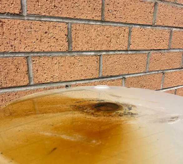 Rust staining around a fitting on the top of a hot water tank beside a brick wall