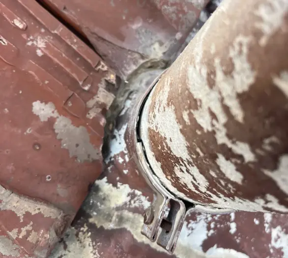 Rusty pipe passing through a tiled roof with a worn flashing collar