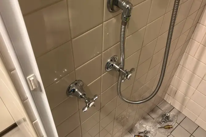 Shower wall with cross-handle taps and hose, with replacement parts on the floor