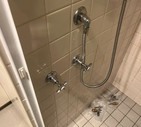 Shower wall with cross-handle taps and hose, with replacement parts on the floor