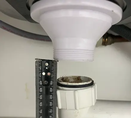 Sink waste pipe under a benchtop with a tape measure held against it