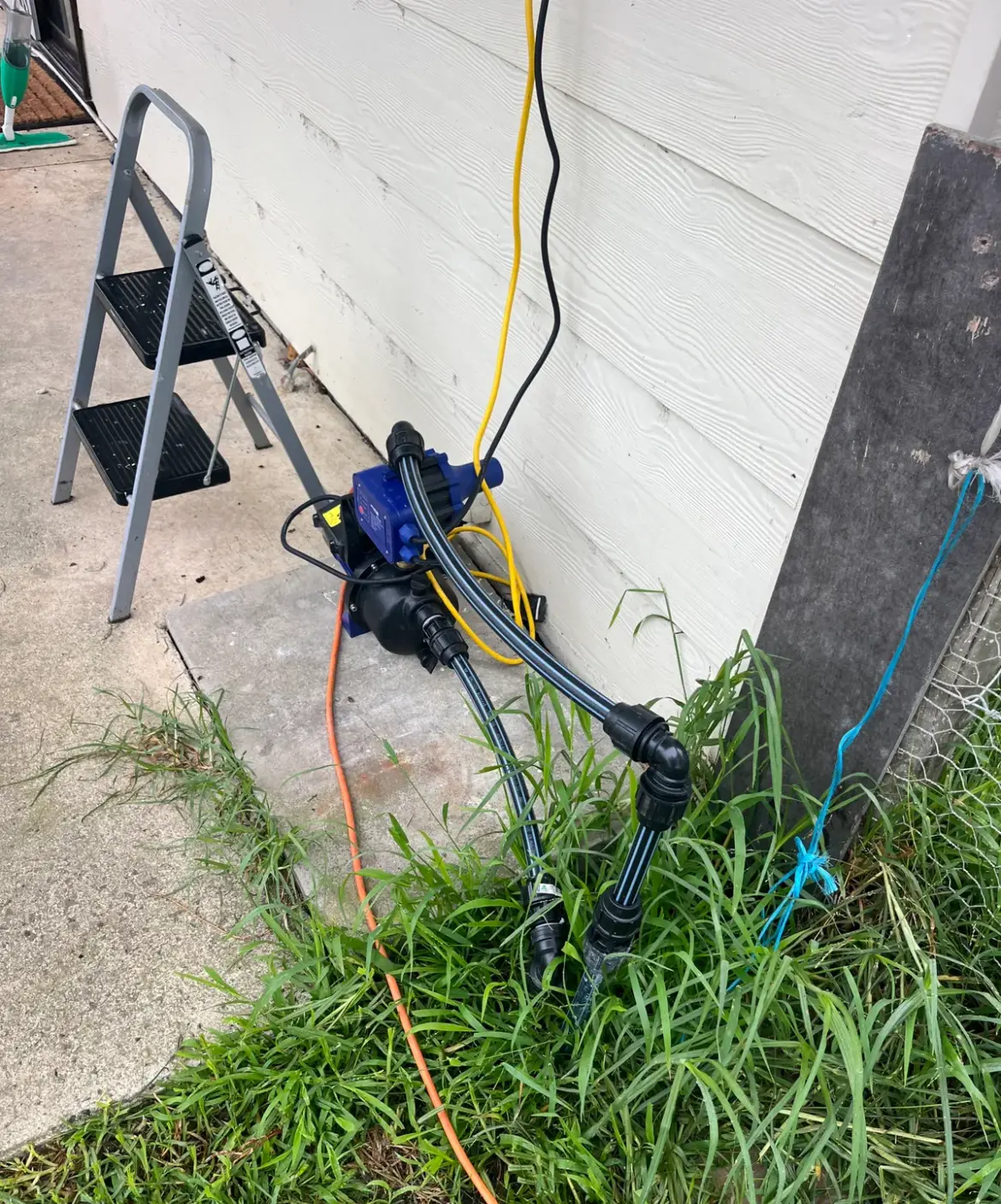 Small blue pump with black poly pipe fittings against an outside wall
