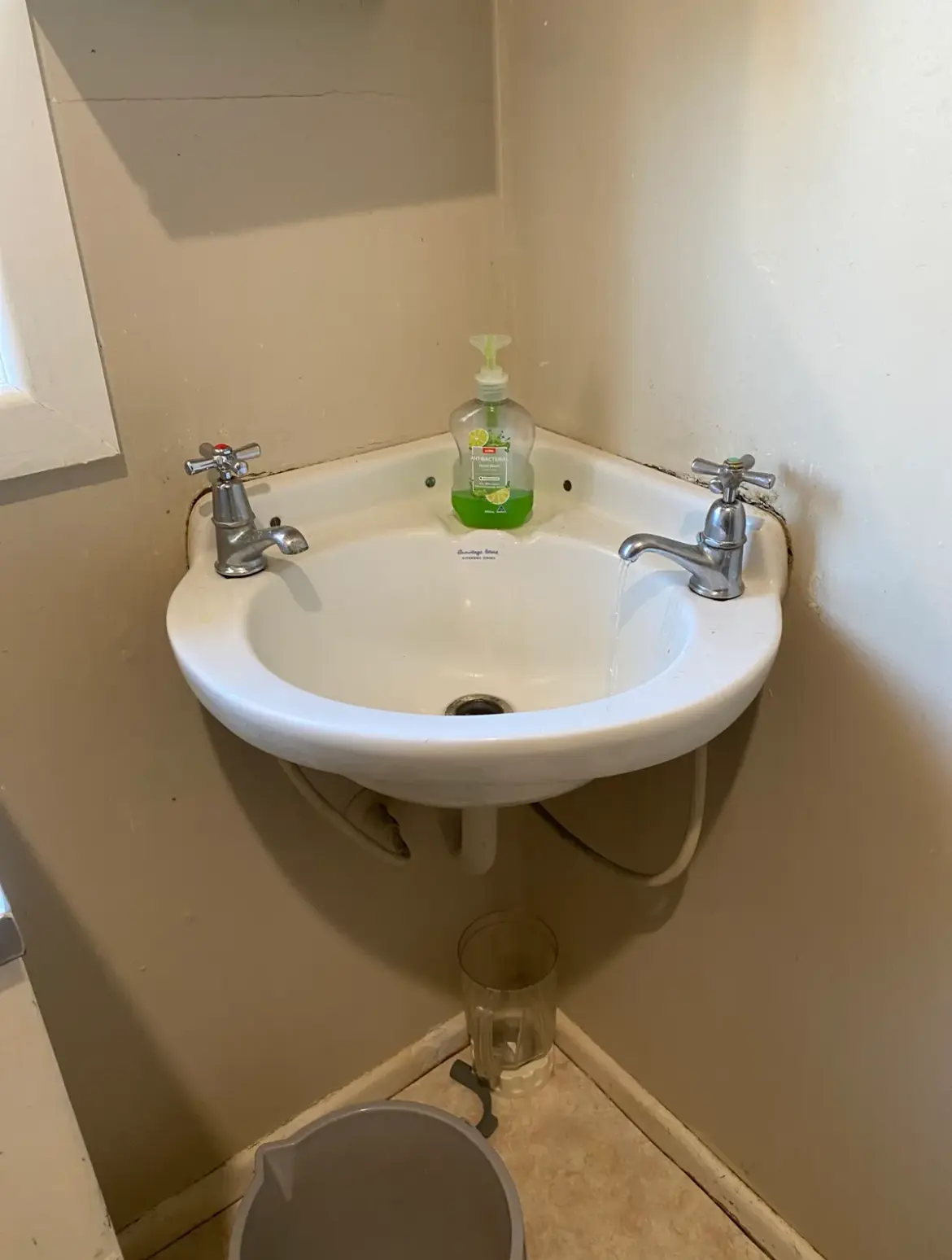 Small corner basin with two chrome cross-handle taps, one running