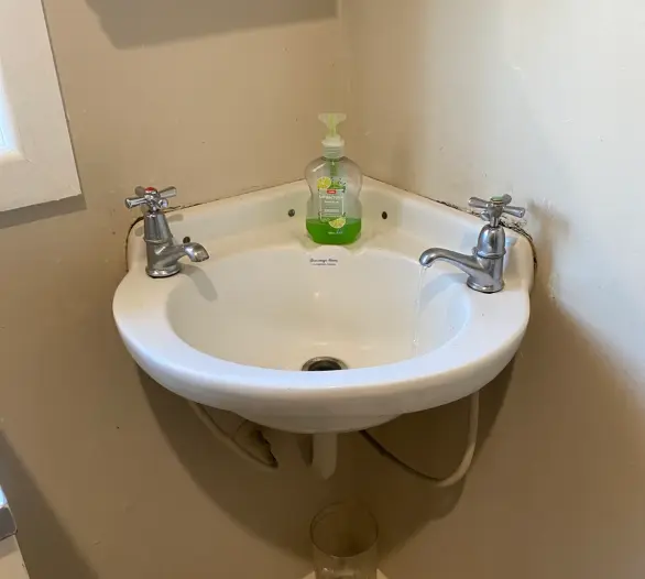 Small corner basin with two chrome cross-handle taps, one running