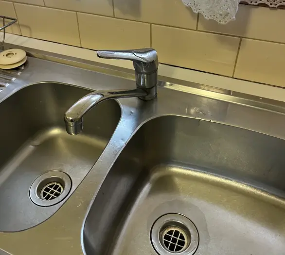 Stainless steel double sink with a swivel mixer tap below a lace curtain