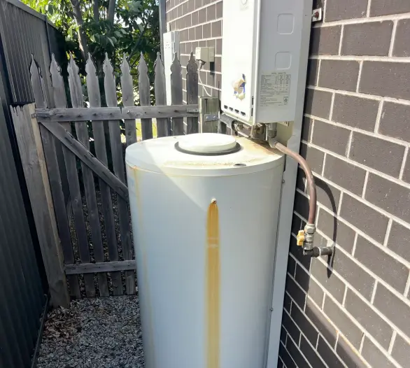Storage hot water tank and continuous flow unit on a dark brick wall beside a gate