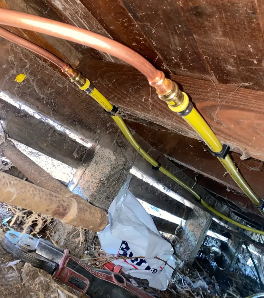 Subfloor copper pipe joined to a yellow gas pipe with tools alongside
