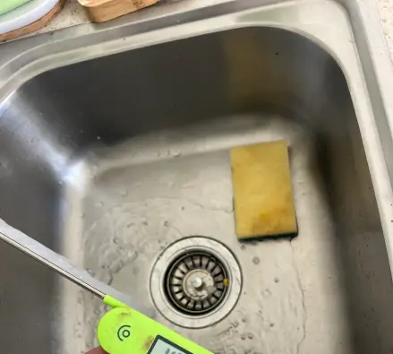 Thermometer in a sink under a running hot tap to test water temperature