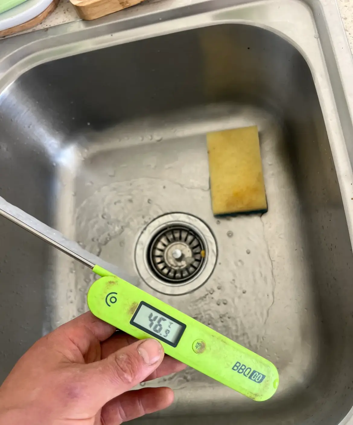 Thermometer in a sink under a running hot tap to test water temperature