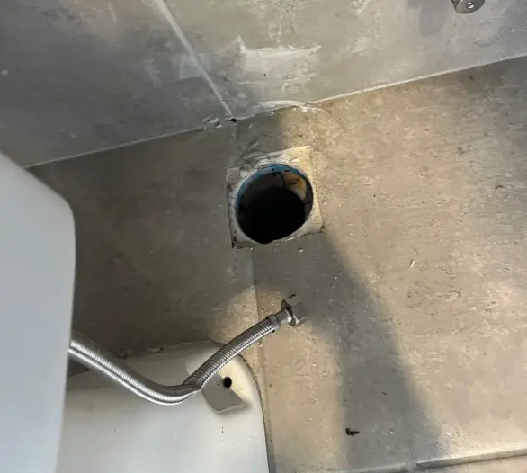 Tiled bathroom wall with an angle stop and an open toilet waste outlet