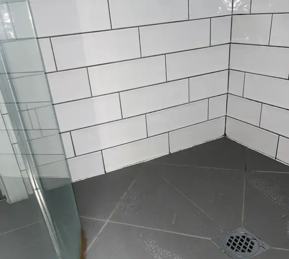 Tiled shower recess with a grey tiled floor, drain and glass screen