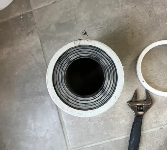 Toilet waste outlet fitted with a pan collar, with a spanner on a tiled floor