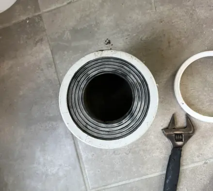 Toilet waste outlet fitted with a pan collar, with a spanner on a tiled floor