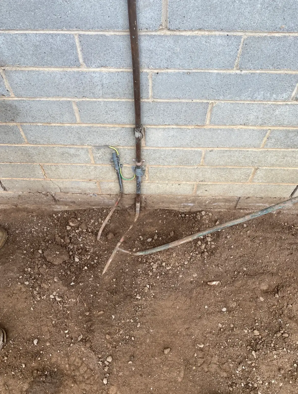 Trench along the base of a block wall with copper and other pipes exposed