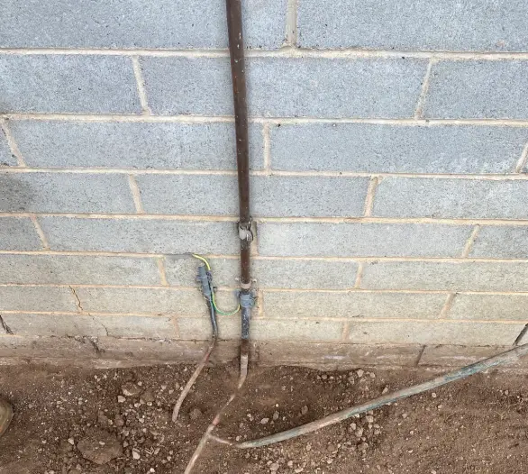 Trench along the base of a block wall with copper and other pipes exposed