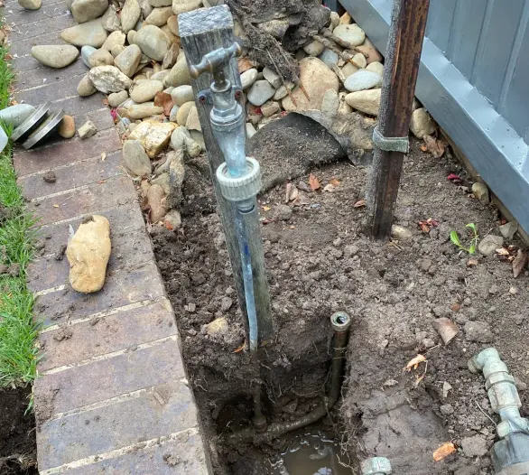 Trench dug beside a brick edge exposing water pipes and brass fittings