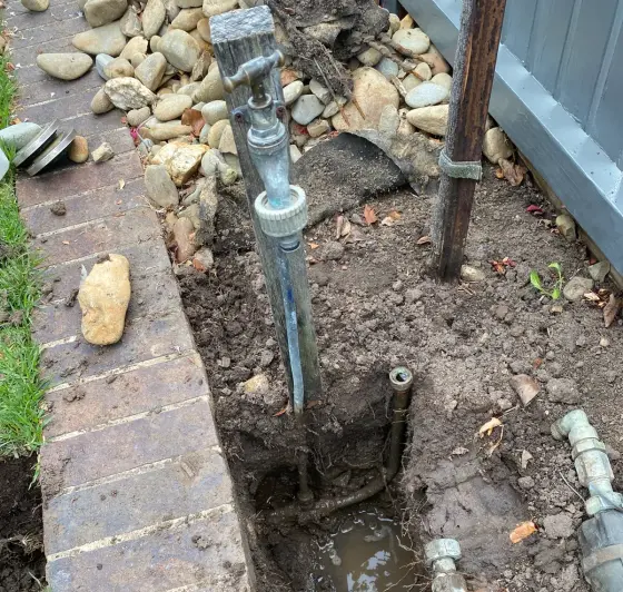 Trench dug beside a brick edge exposing water pipes and brass fittings