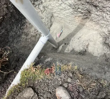 Trench with a white PVC pipe and a work boot at the edge