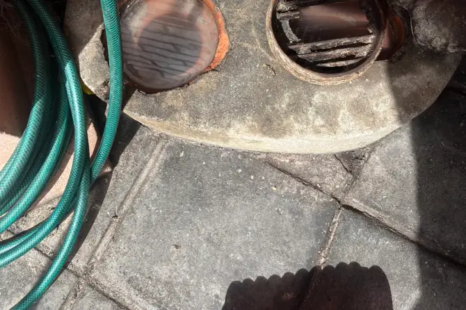 Two round drain openings set in a concrete base against a brick wall, with a garden hose coiled beside them