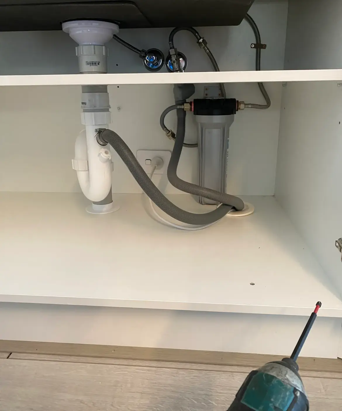 Under-sink water filter housing with hoses and angle stops, with a cordless drill in view