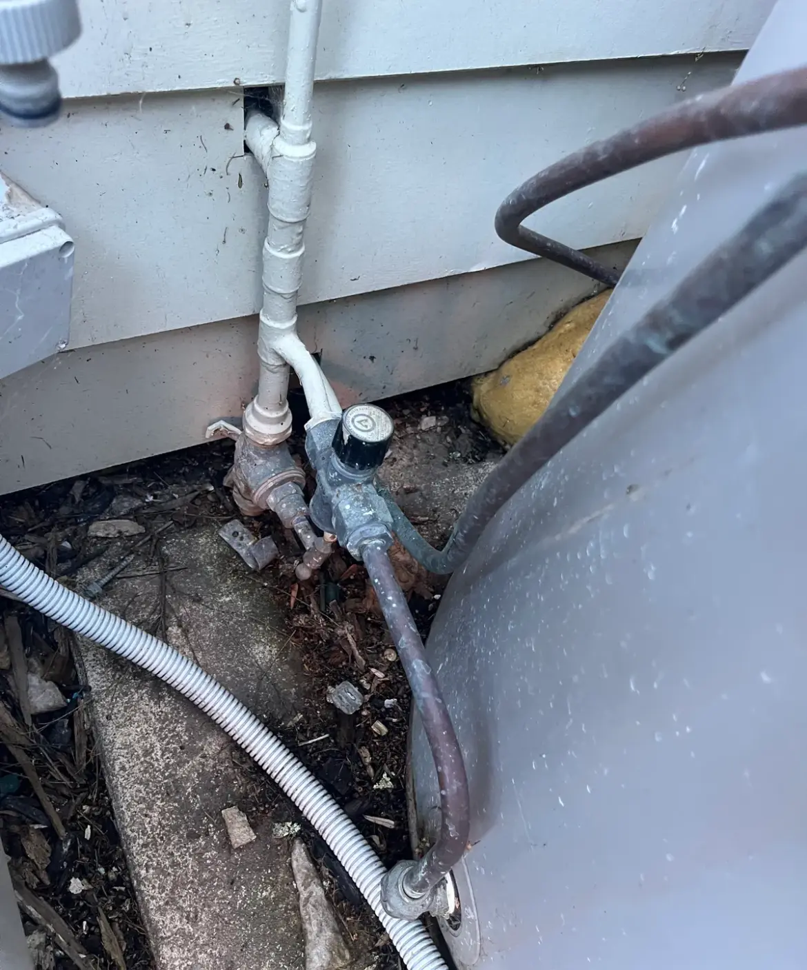 Valves and copper pipework between a weatherboard wall and a hot water unit